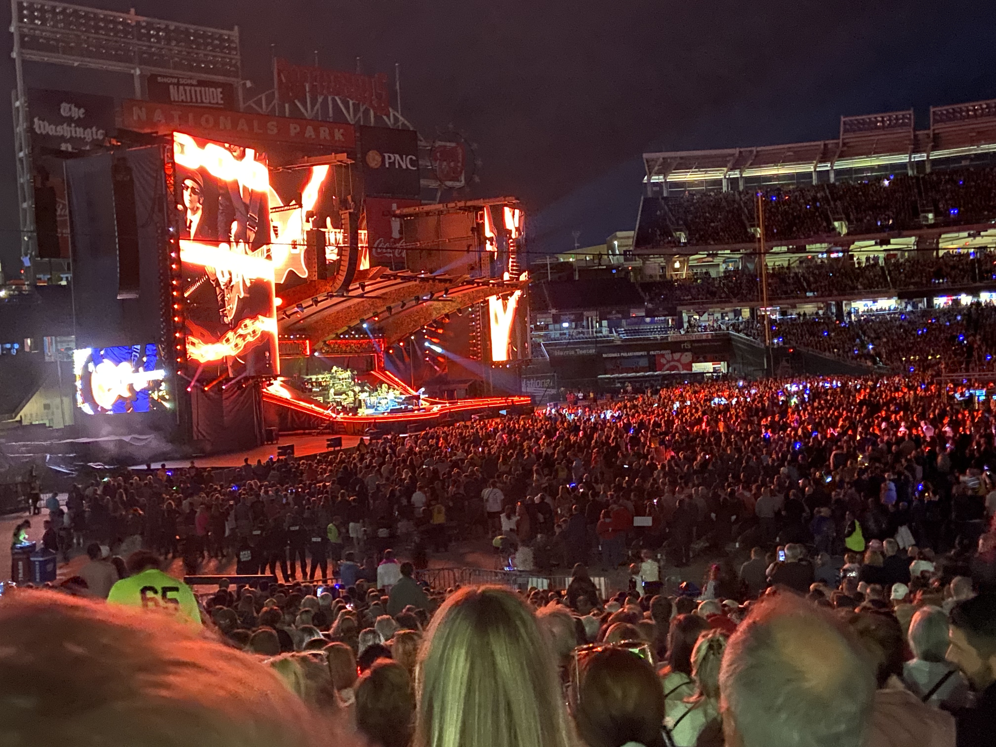 Elton John se apresentando ao piano em um show, com luzes coloridas ao fundo